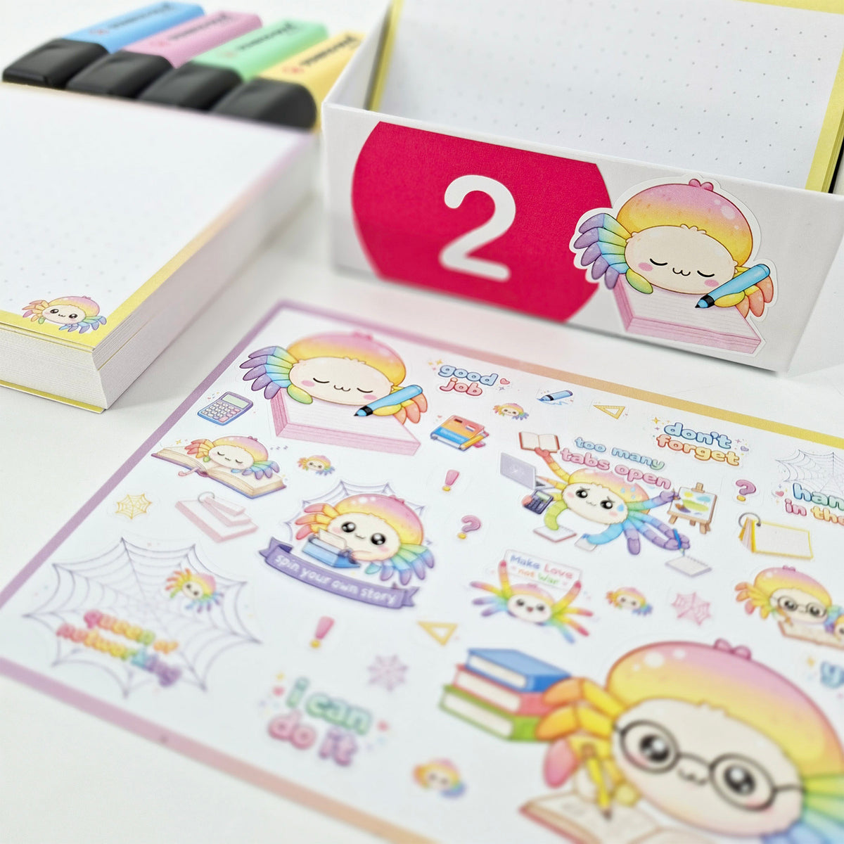 A sheet of cute pastel school-themed stickers is displayed in the foreground, with matching sticker boxes and colorful markers in the background on a white surface.